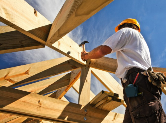 Carpenter hammering a nail into the frame of a custom built house
