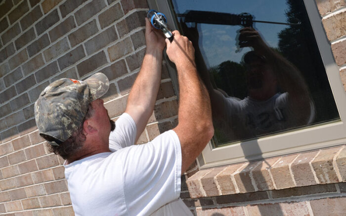 Man applying caulk to a window in a brick building